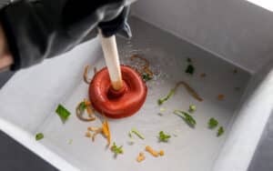 A plumber clears a clogged kitchen sink using a plunger to address a drain clog.