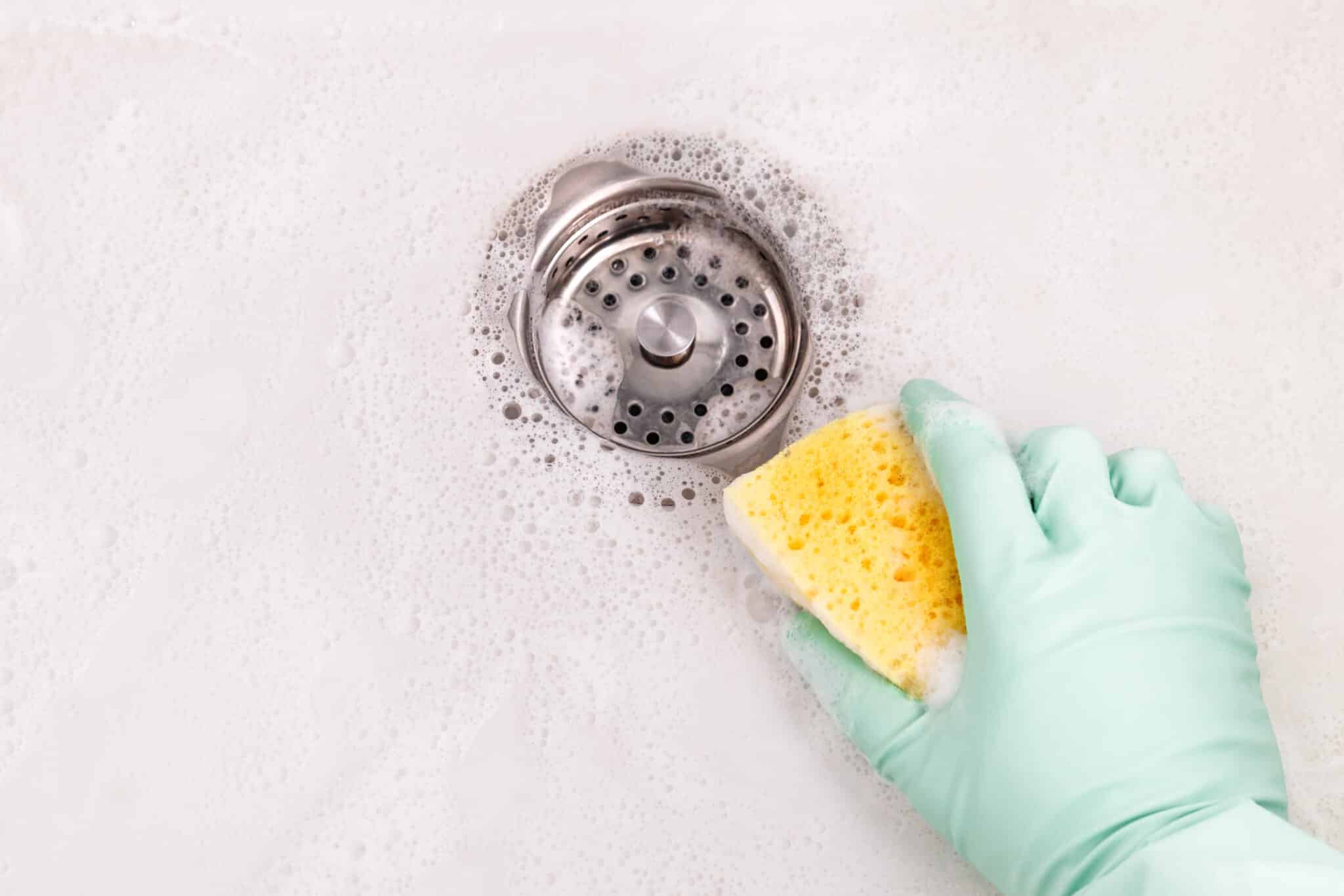 Person hand holding a yellow sponge, cleaning sink, Chronic Drain Issues.